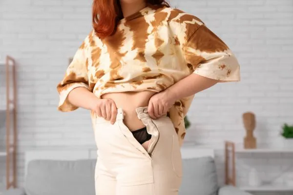 Image of woman trying to do her trousers up after pregnancy weight gain Sherborne
