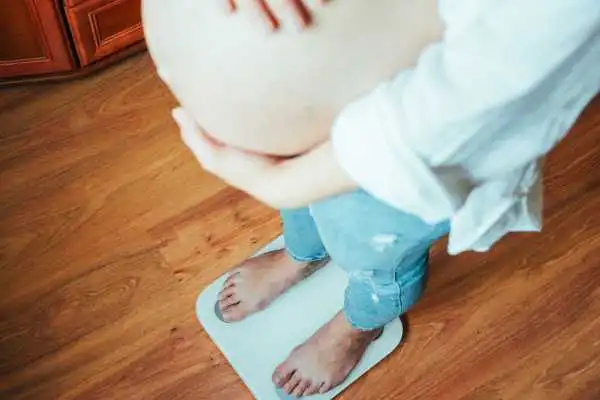 Image of woman weighing herself and experiencing weight gain through pregnancy Sherborne